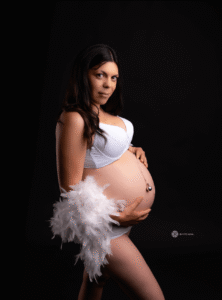 Retrato elegante de mujer embarazada con fondo negro y plumas blancas, sesión premamá en JS Foto Albal, estudio en Albal (Valencia).
